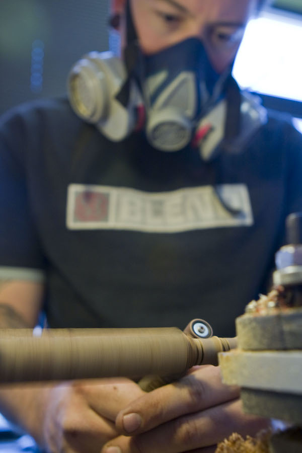 Craftsman using hand Dremel to sand wood ear gauge jewelry on a lathe. 